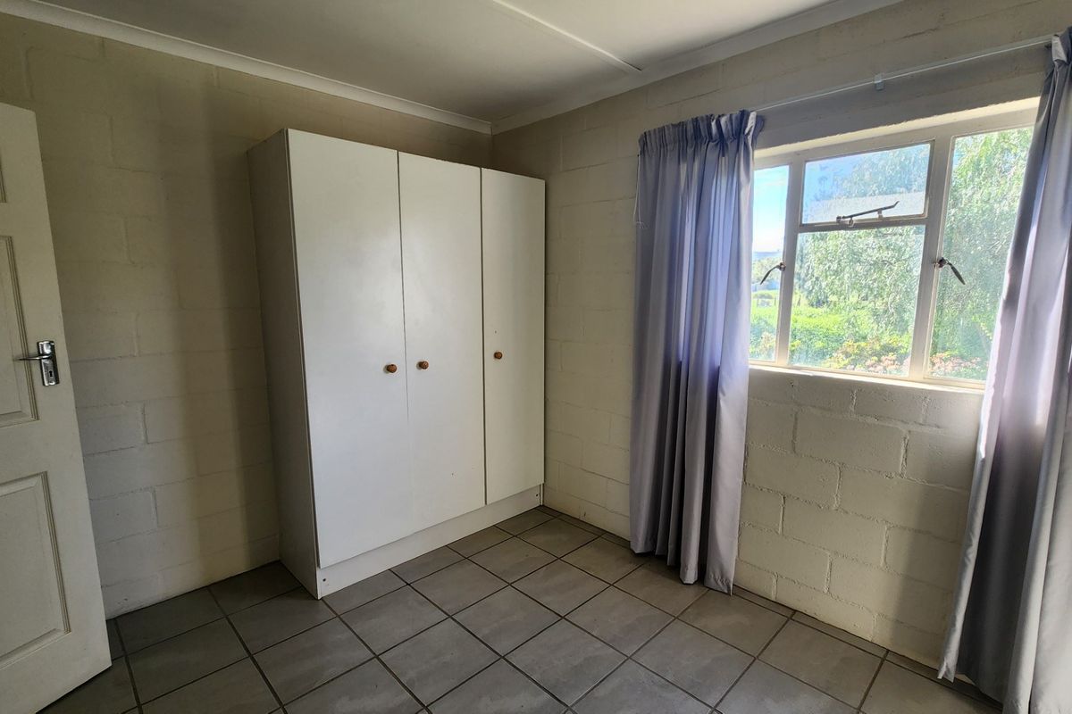 A functional bedroom featuring tiled flooring, exposed cinder block walls, and a built-in wardrobe, offering a neutral canvas for potential updates.