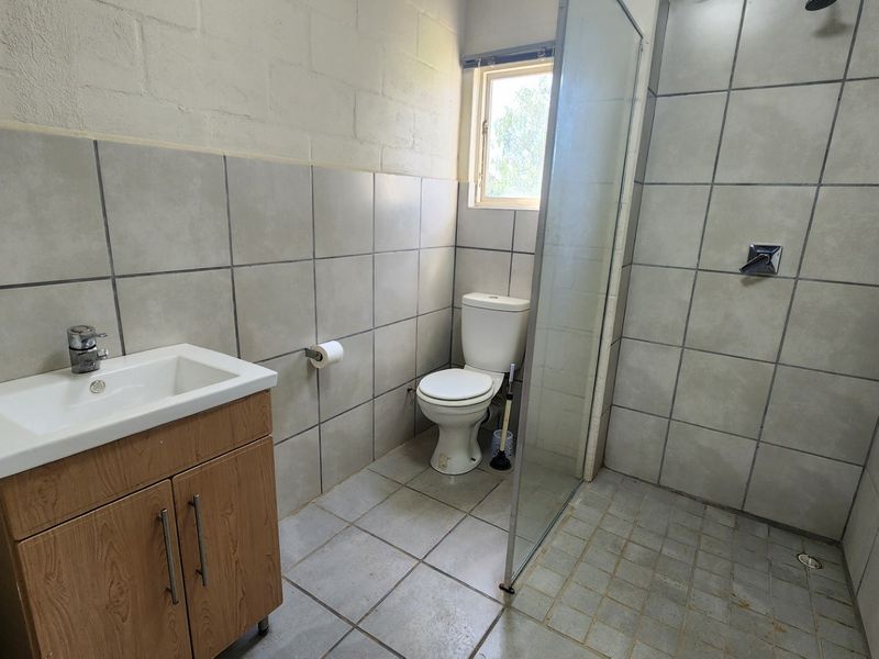 A functional bathroom featuring a vanity cabinet, toilet, and a glass-enclosed shower with neutral tiled finishes.