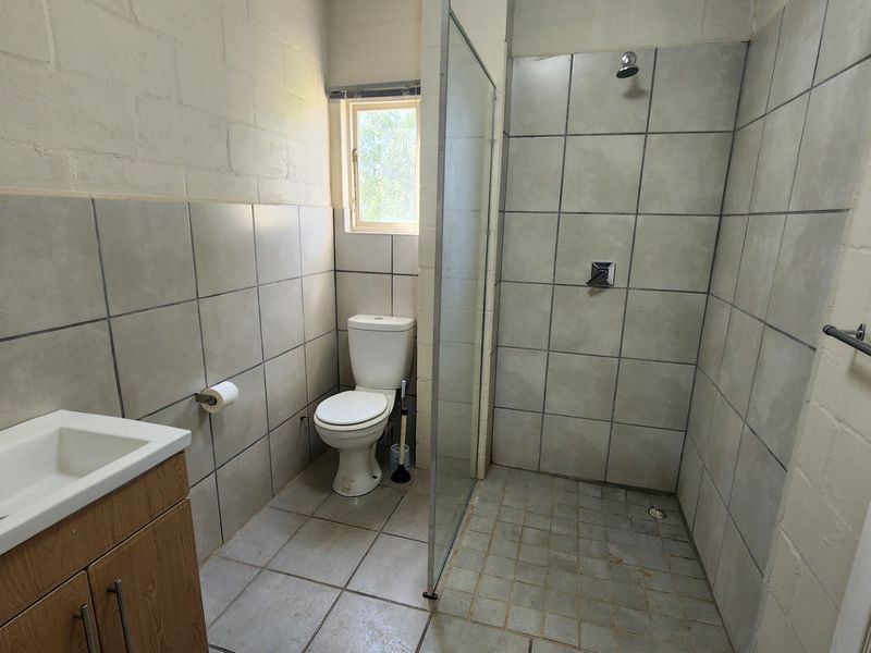 A functional bathroom featuring a vanity basin, toilet, and a walk-in shower with a glass screen and tiled finishes.
