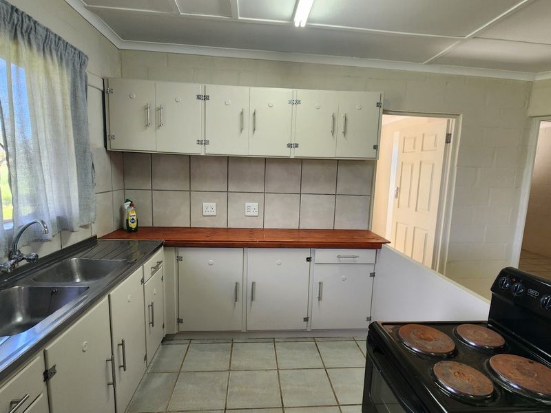 A functional kitchen featuring built-in cabinetry, a double bowl sink, tiled splashbacks, and a timber countertop, requiring cosmetic updates to modernize the space.