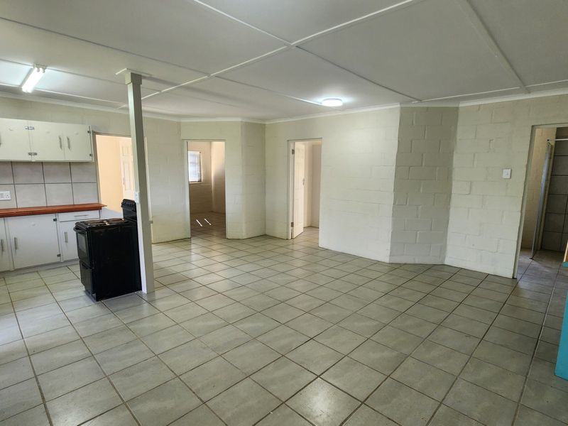 Open-plan living and kitchen area featuring tiled flooring, exposed blockwork walls, and dated built-in cabinetry, offering a blank canvas for renovation.