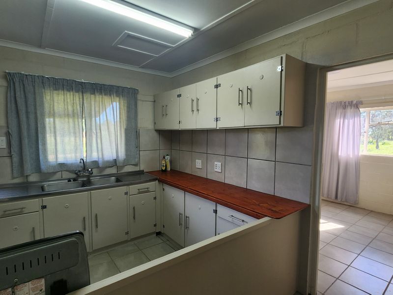 A functional kitchen featuring built-in cabinetry, a double basin sink, and a wooden countertop, with direct access to an adjacent room.