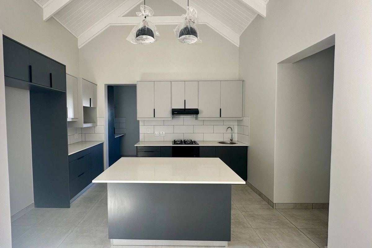 Modern kitchen featuring a central island, quartz countertops, two-tone cabinetry, gas hob, and a high vaulted ceiling with exposed rafters.