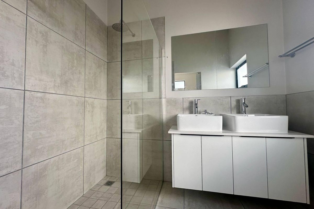Modern bathroom featuring a double vanity with white cabinetry, a spacious walk-in shower with glass screen, and contemporary grey wall tiles.