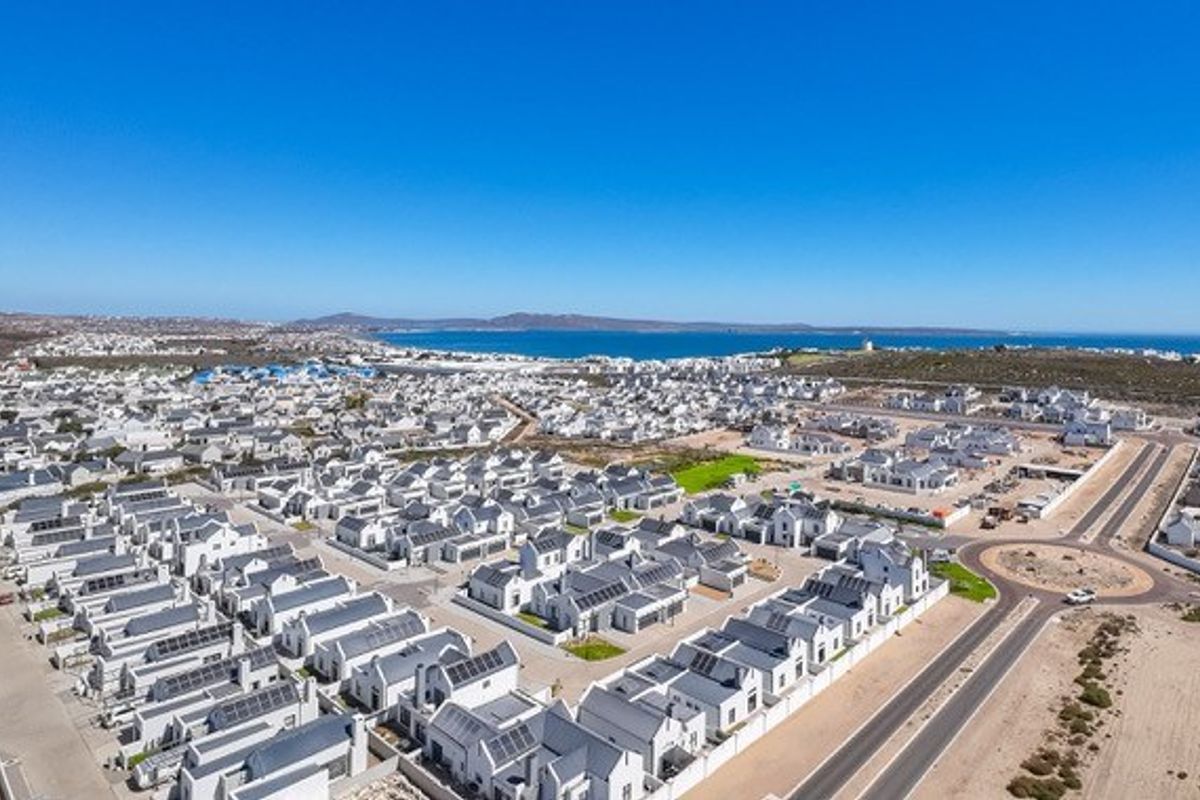 An aerial view of a modern residential estate featuring uniform housing with solar panels, situated near the coastline.