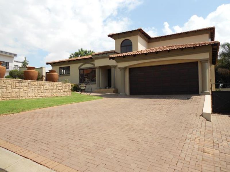 Front elevation of a double-story residence featuring a paved driveway, double garage, and stone retaining wall with landscaped garden.