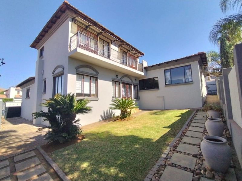 A well-maintained two-story residential property featuring a rear garden, paved walkway, and an upper-level balcony with wrought iron railings.