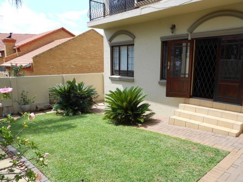 A well-maintained rear garden featuring a paved patio area, tiled steps leading to the house, and a balcony with wrought iron railings.