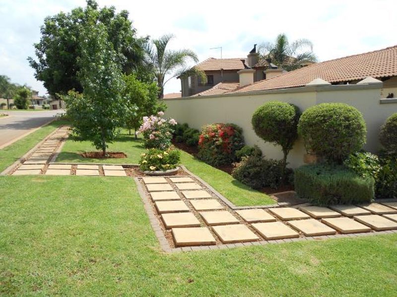 A well-maintained front garden featuring a paved walkway, manicured shrubs, and a solid boundary wall.