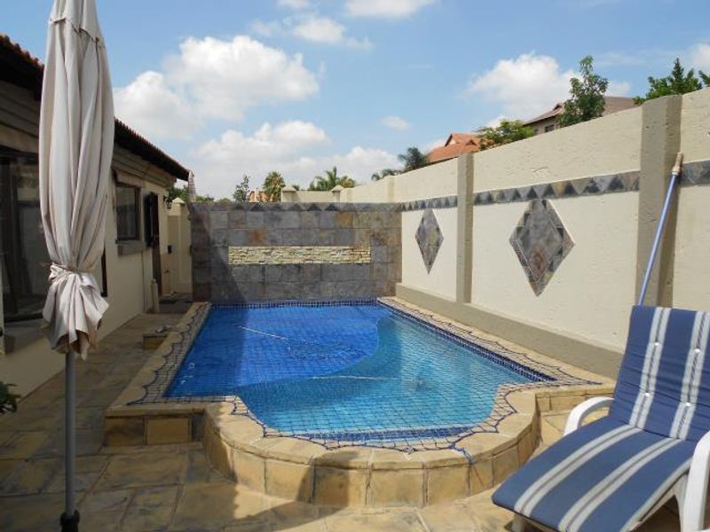 A compact swimming pool area featuring a decorative stone feature wall, tiled surround, and a protective safety net, enclosed by a high boundary wall.