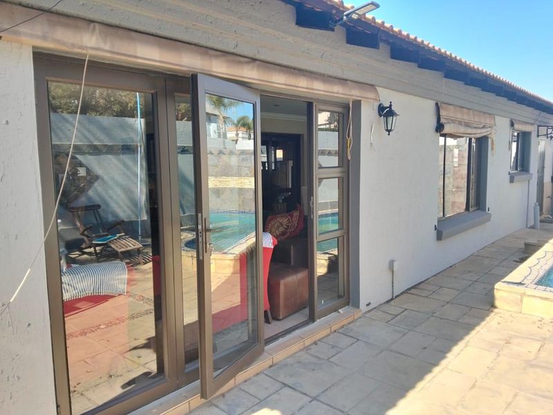 Rear exterior view of the property featuring a paved patio area, aluminium sliding doors, and a view of the swimming pool.