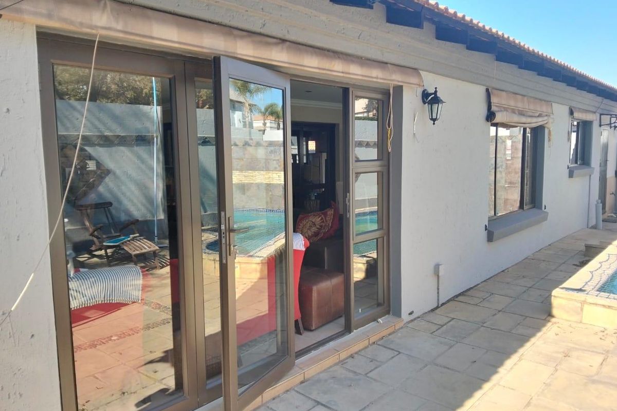Rear exterior view of the property featuring a paved patio area, aluminium sliding doors, and a view of the swimming pool.