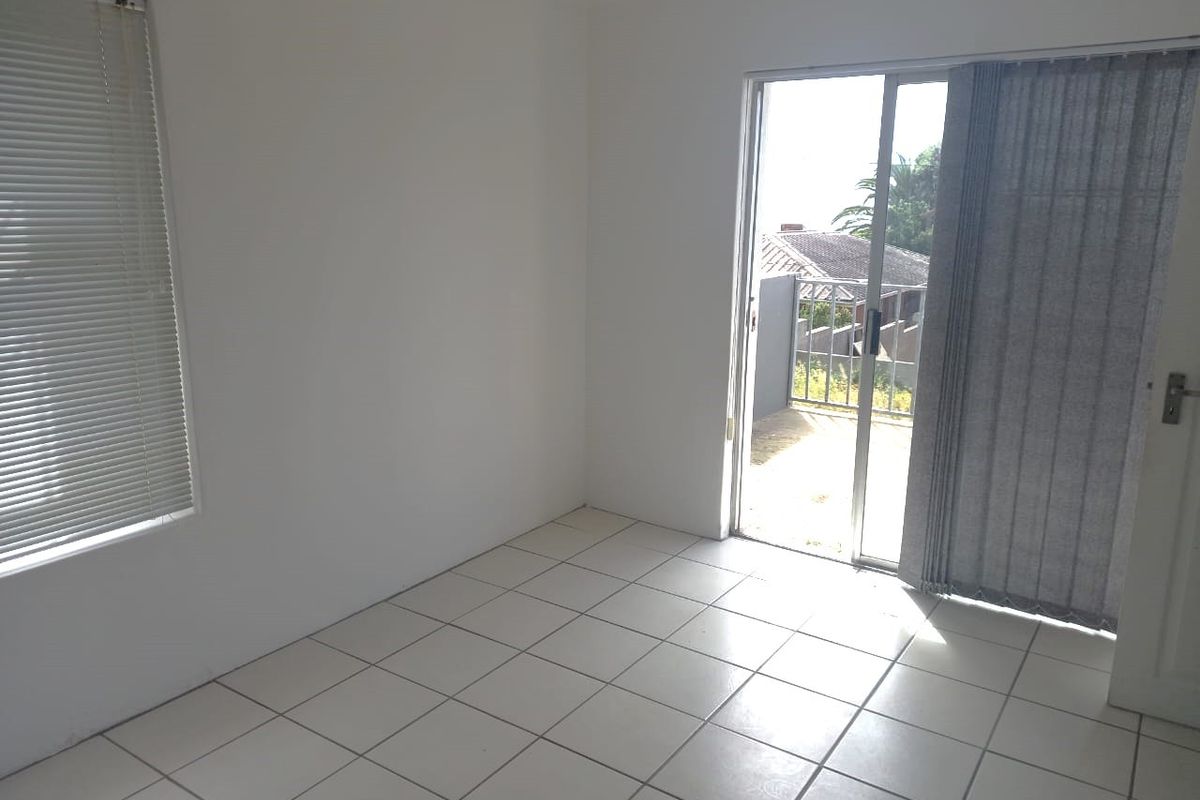 An empty bedroom featuring tiled flooring, a sliding glass door leading to a balcony, and neutral white walls.