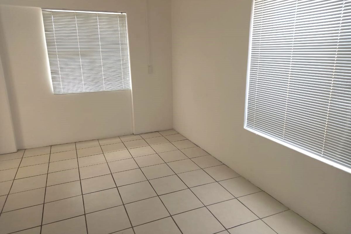 A bright, empty bedroom featuring neutral tiled flooring and fitted venetian blinds on the windows, offering a clean canvas for personalization.