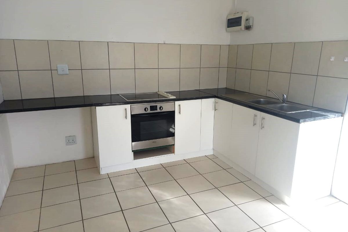 A functional kitchen featuring white cabinetry, dark countertops, a built-in oven, electric hob, and a double sink with tiled splashbacks.