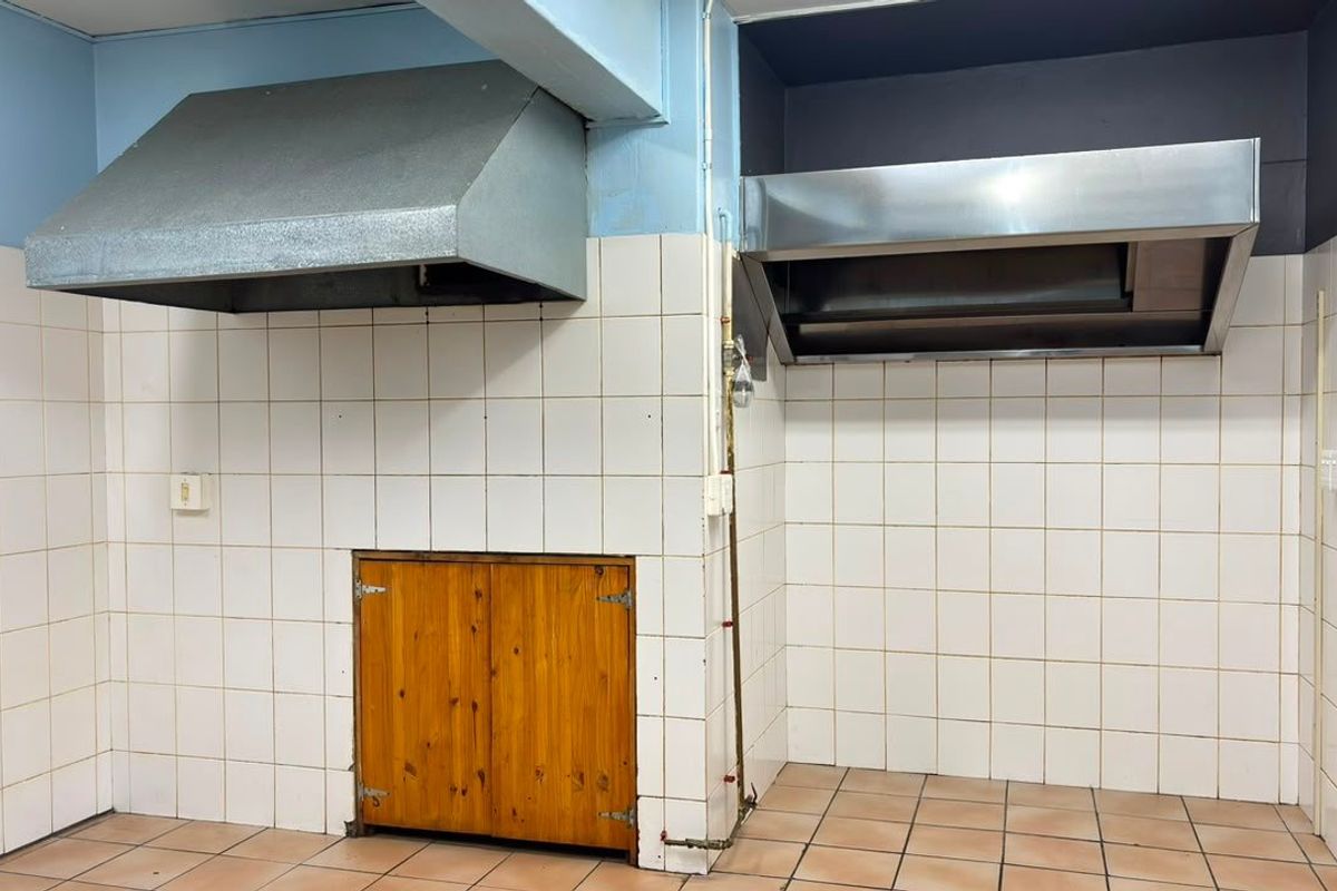 Commercial kitchen area featuring dual stainless steel extractor hoods, tiled walls, and tiled flooring, suitable for professional food preparation.