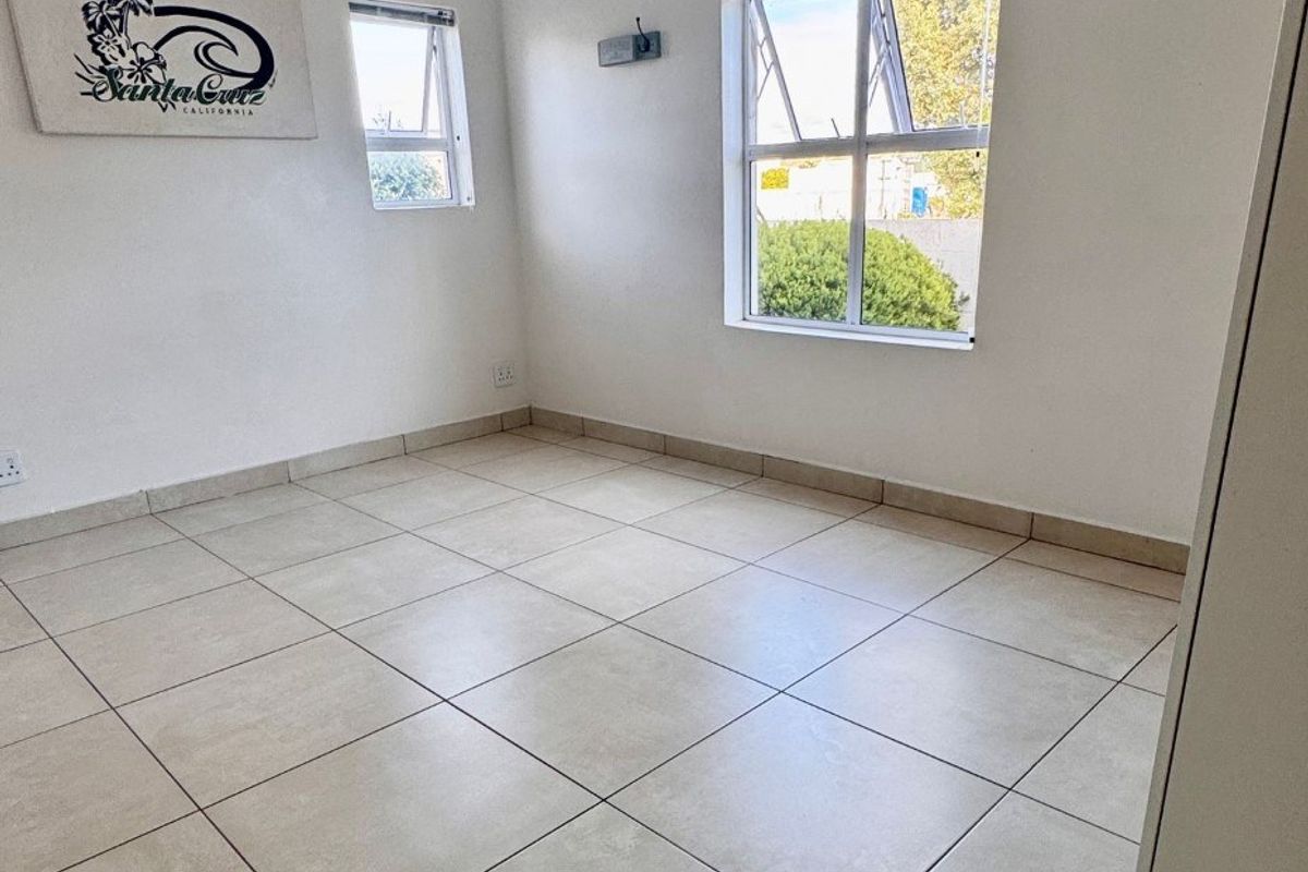 A bright, empty bedroom featuring neutral floor tiles, clean white walls, and natural light from multiple top-hung windows.