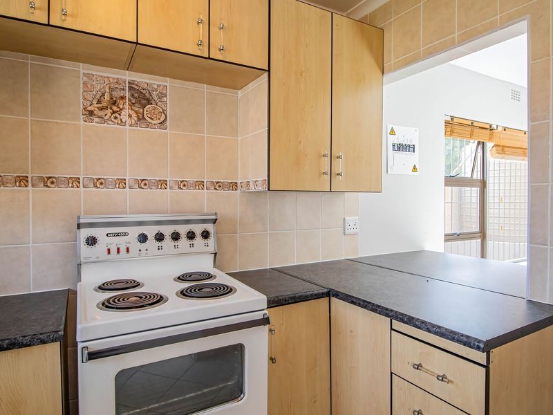 Functional kitchen featuring light wood-finish cabinetry, laminate countertops, a freestanding electric stove, and a convenient pass-through window to the adjacent living area.
