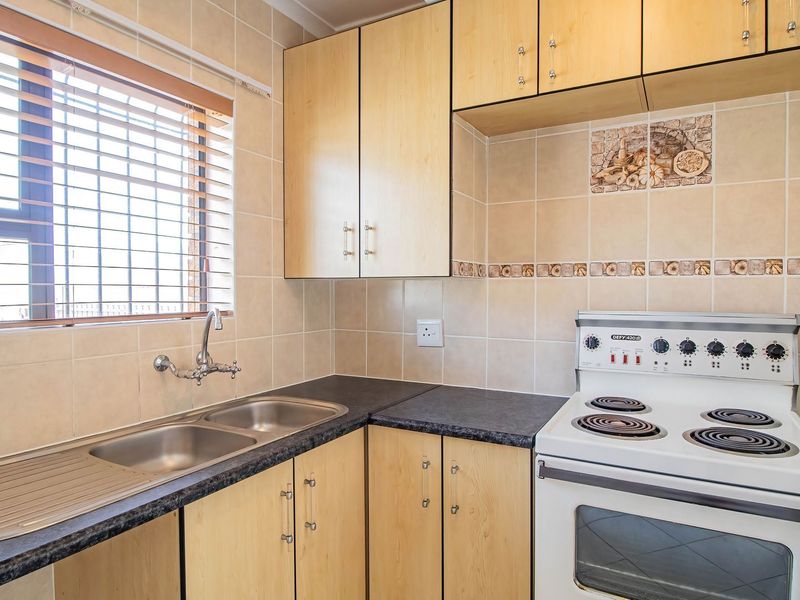 A functional kitchen featuring light wood-finish cabinetry, a double stainless steel sink, tiled splashbacks, and a freestanding electric stove.