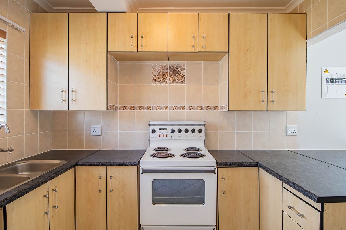 A functional kitchen featuring light wood-finish cabinetry, dark laminate countertops, a double stainless steel sink, and a freestanding electric stove with tiled backsplash.