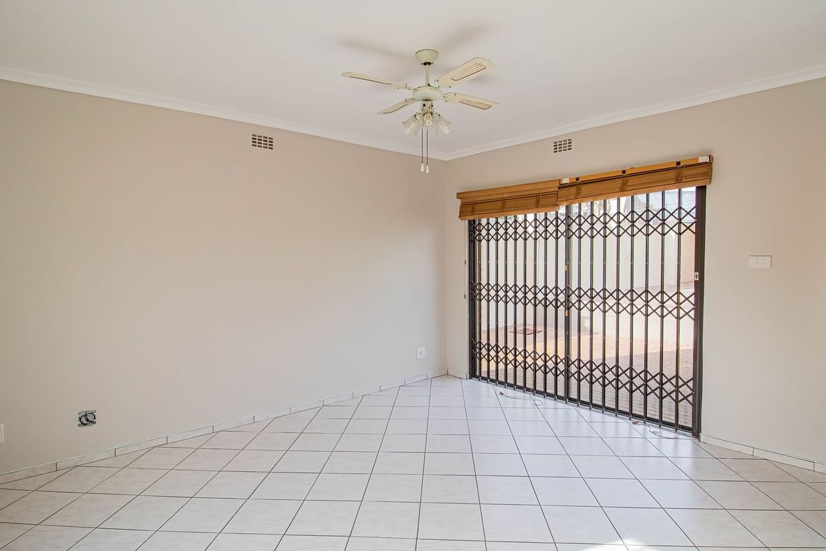 An empty living room featuring tiled flooring, a ceiling fan, and a sliding door with a security gate leading to the exterior.