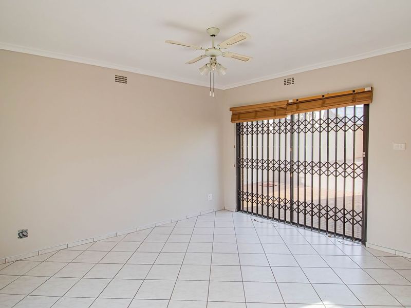 An empty living room featuring tiled flooring, a ceiling fan, and a sliding door with a security gate leading to the exterior.