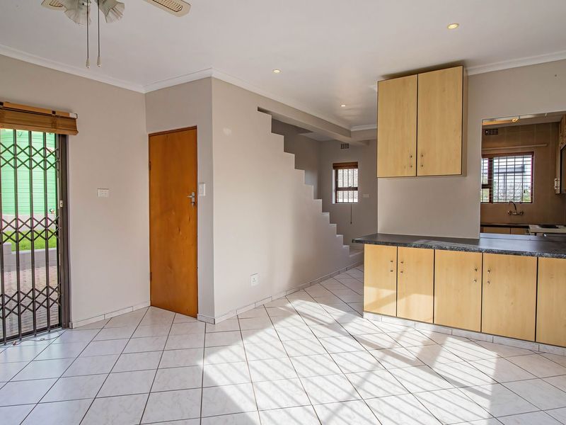 Open-plan living and kitchen area featuring tiled floors, light wood cabinetry, laminate countertops, and direct access to an outdoor patio through a security gate.