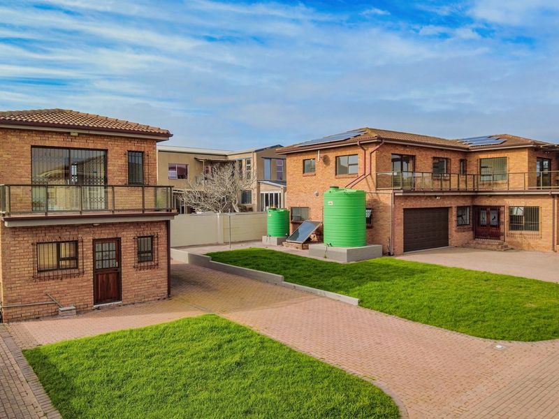 Aerial view of a face brick property featuring a paved courtyard, green lawn, water storage tanks, solar heating, and upper-level balconies.
