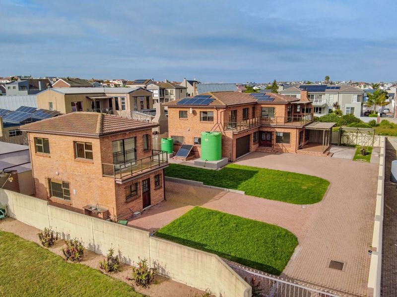 Aerial view of a residential property featuring two brick buildings, paved driveway, green lawns, solar panels, and water storage tanks.