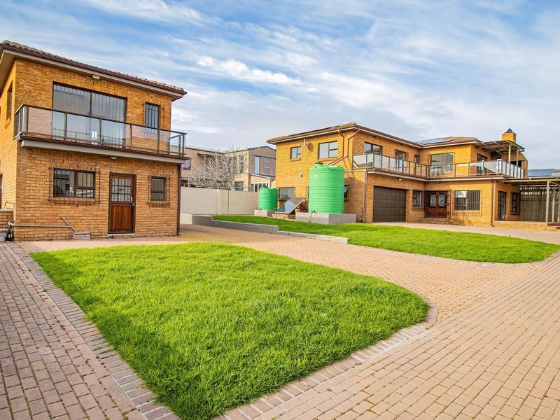 Exterior view of the property featuring face brick buildings, paved driveway, balconies with glass balustrades, and installed water storage tanks.