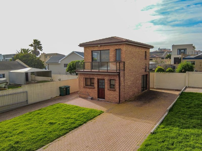 Aerial view of a two-story detached brick property featuring a balcony, paved driveway, and surrounding garden area.
