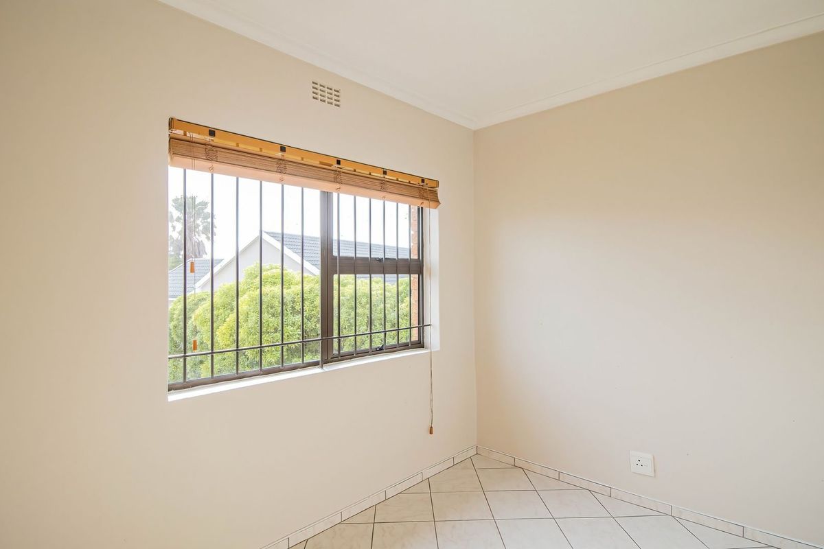 A bright, empty bedroom featuring neutral walls, tiled flooring, and a window fitted with security bars.