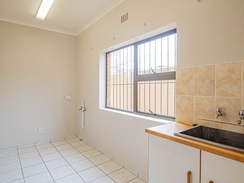A functional laundry room featuring tiled flooring, a stainless steel sink with tiled splashback, and dedicated plumbing connections for appliances.