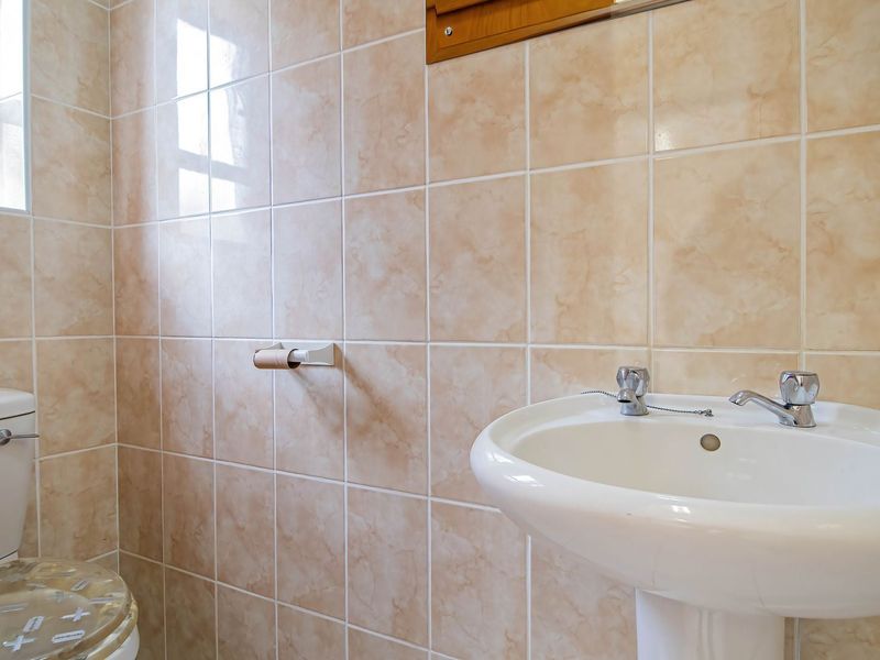 A functional bathroom featuring a pedestal basin with dual-handle faucets and full-height ceramic wall tiling.