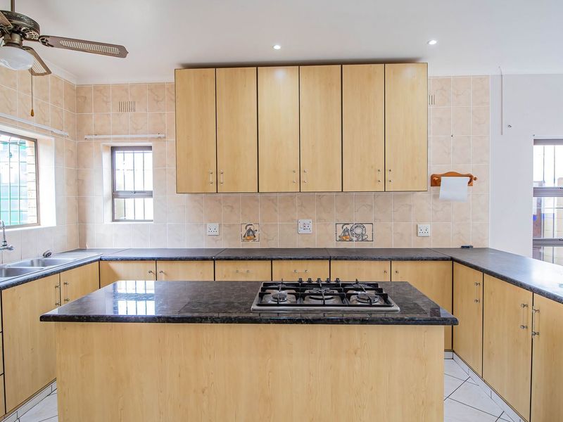 A spacious kitchen featuring light wood cabinetry, dark laminate countertops, a central island with a gas hob, and tiled backsplash throughout.