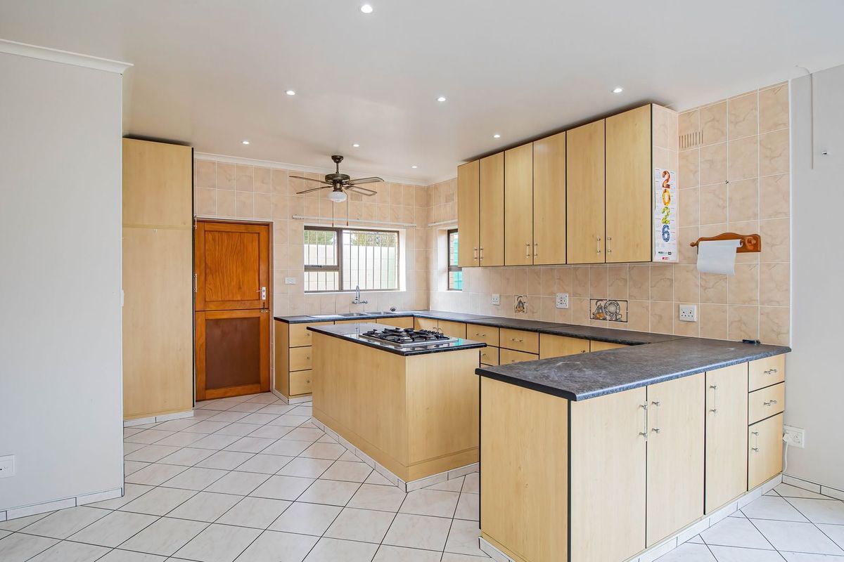 A spacious kitchen featuring light wood cabinetry, dark laminate countertops, a central island with a gas hob, and tiled flooring throughout.
