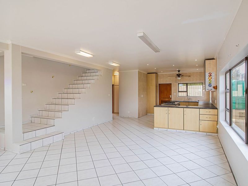 Spacious open-plan living area featuring a tiled staircase, neutral finishes, and a functional kitchen with built-in cabinetry and island cooktop.