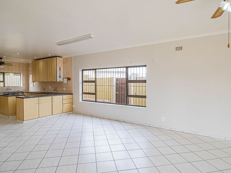 Spacious open-plan kitchen and living area featuring tiled flooring, built-in cabinetry, and large windows with security bars.