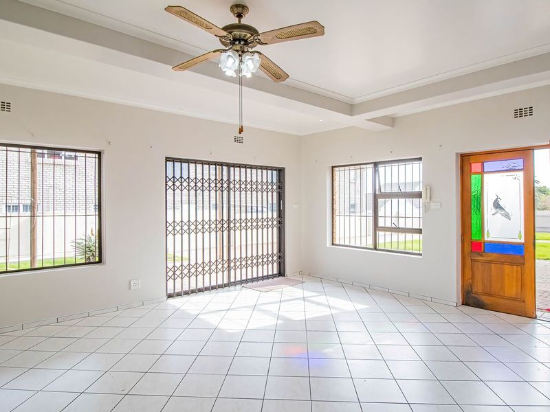 Spacious living area featuring tiled flooring, a ceiling fan, recessed ceiling details, and secure access via a decorative stained glass door and security gates.