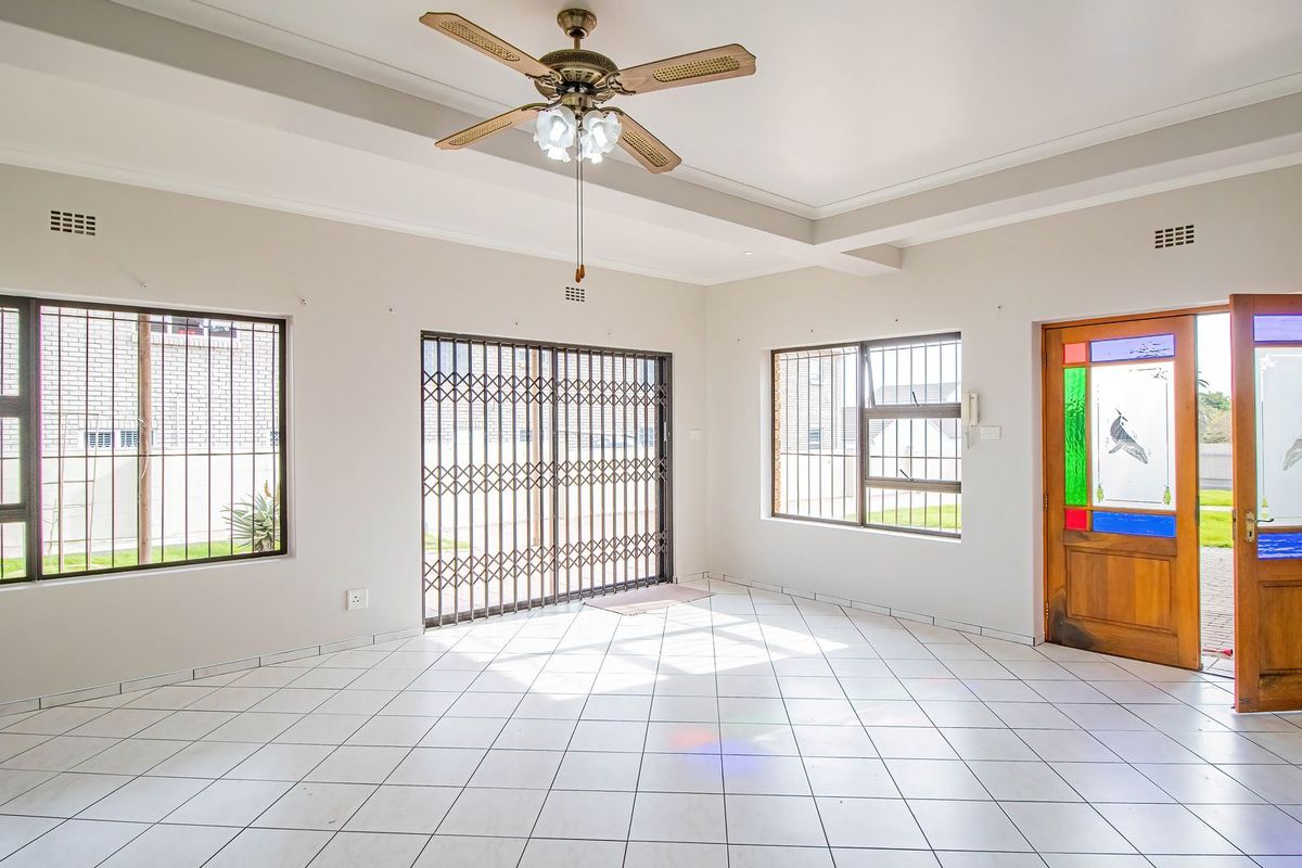 Spacious living area featuring tiled flooring, a ceiling fan, recessed ceiling details, and secure access via a decorative stained glass door and security gates.