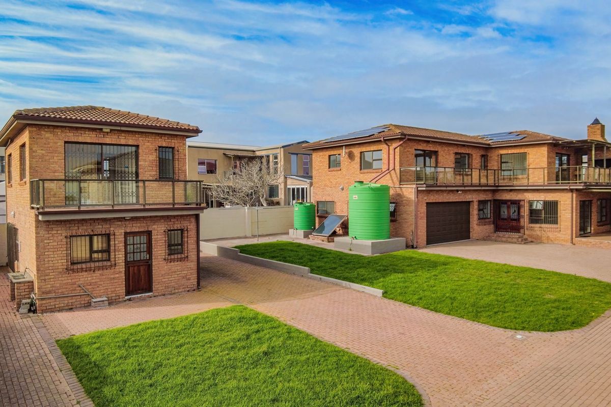 Aerial view of a face brick property featuring a paved courtyard, lawn, water storage tanks, solar heating, and a balcony.