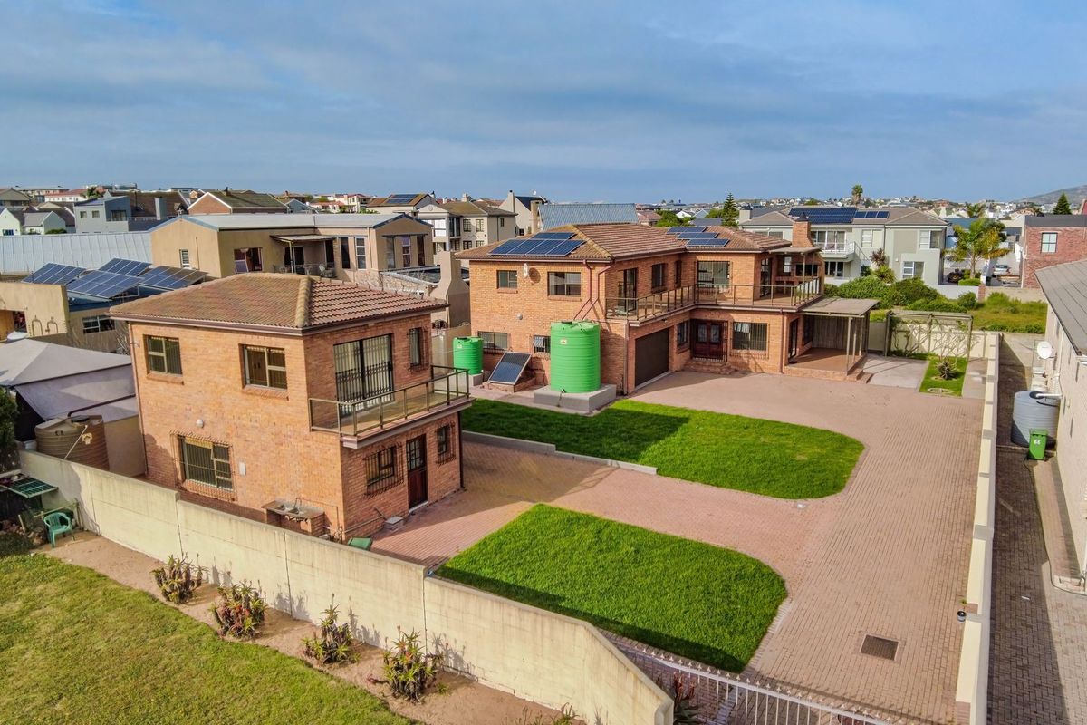 Aerial view of a residential property featuring two brick buildings, solar panels, water tanks, a paved driveway, and landscaped lawn areas.