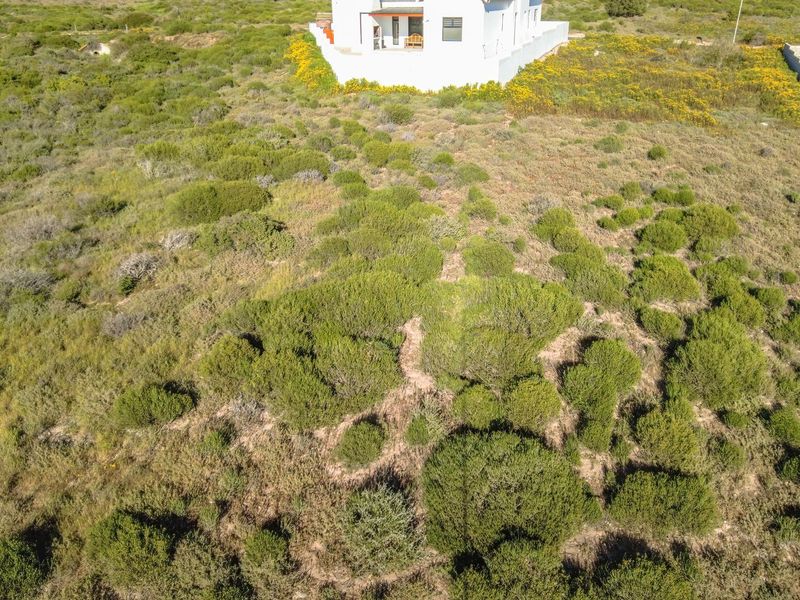 An aerial view of a vacant residential plot featuring natural coastal vegetation with an adjacent house visible in the background.