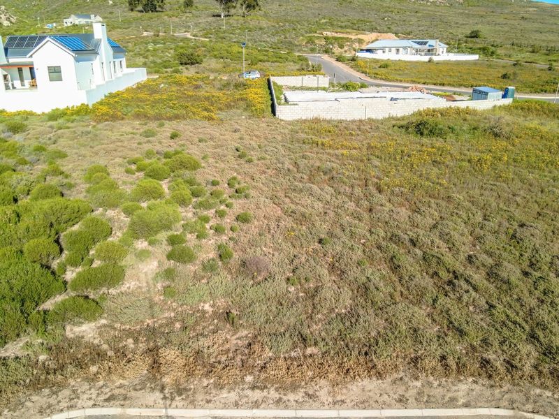 Aerial view of a vacant residential plot featuring natural vegetation and a partial boundary wall in a developing neighborhood.