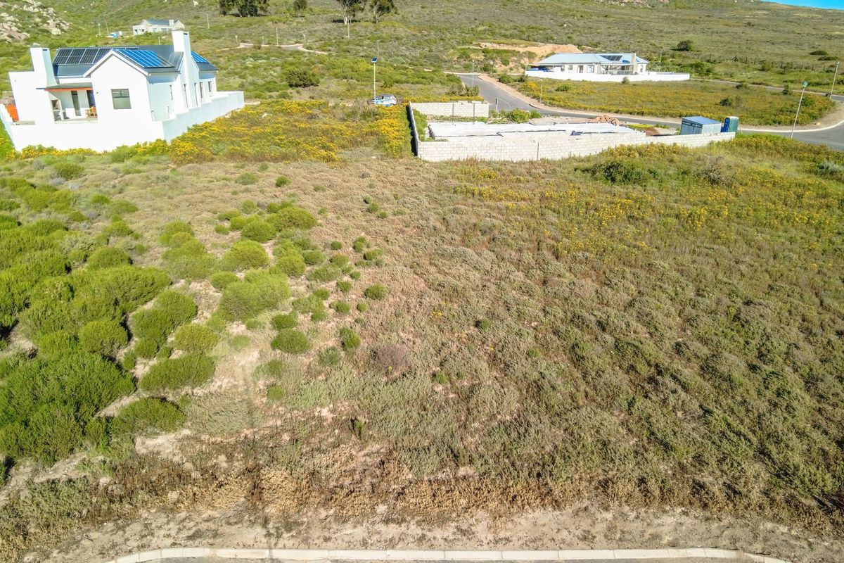 Aerial view of a vacant residential plot featuring natural vegetation and a partial boundary wall in a developing neighborhood.