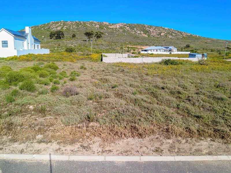 A vacant residential plot featuring natural vegetation, a concrete block boundary wall, and scenic mountain views in a quiet neighborhood setting.