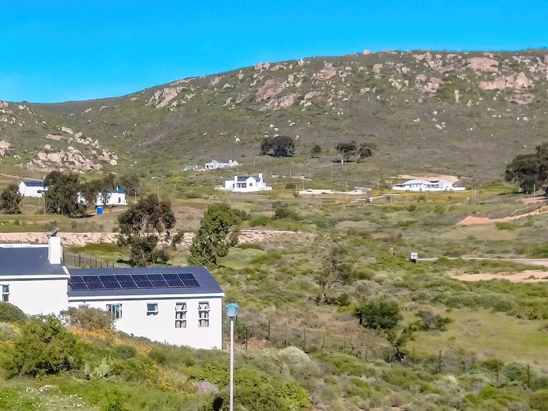 A scenic elevated view of the residential estate landscape featuring natural terrain, scattered homes, and solar panel installations.