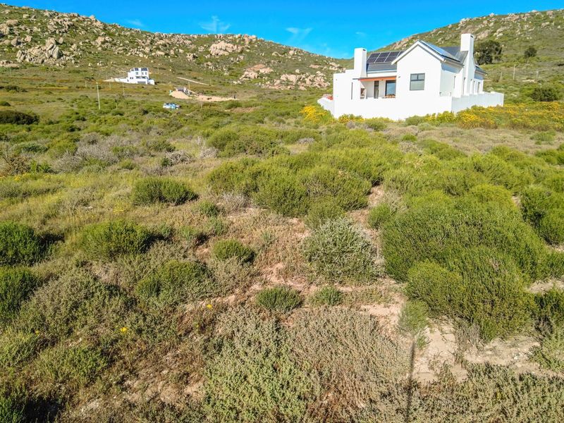 Aerial view of a residential property situated on a large, undeveloped plot of land with natural vegetation and mountainous surroundings.