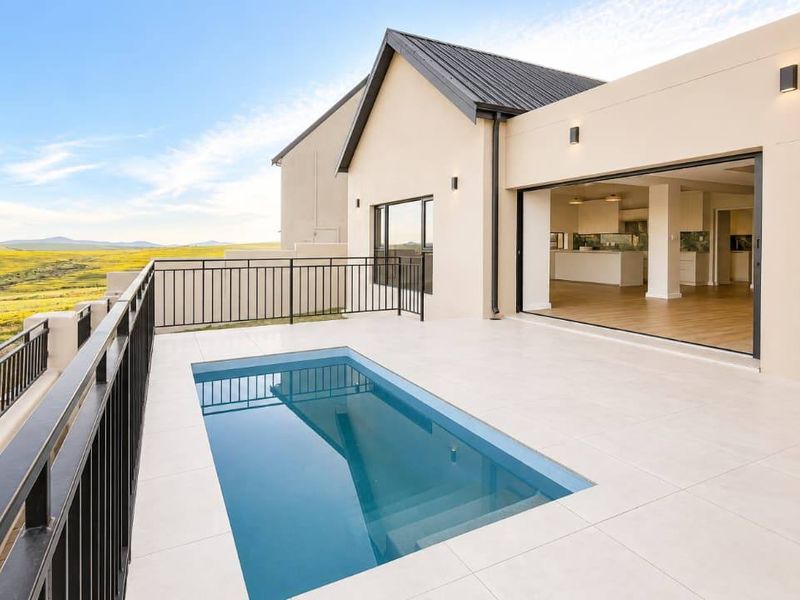Modern outdoor patio featuring a swimming pool, metal balustrades, and seamless indoor-outdoor flow through large sliding glass doors with expansive landscape views.