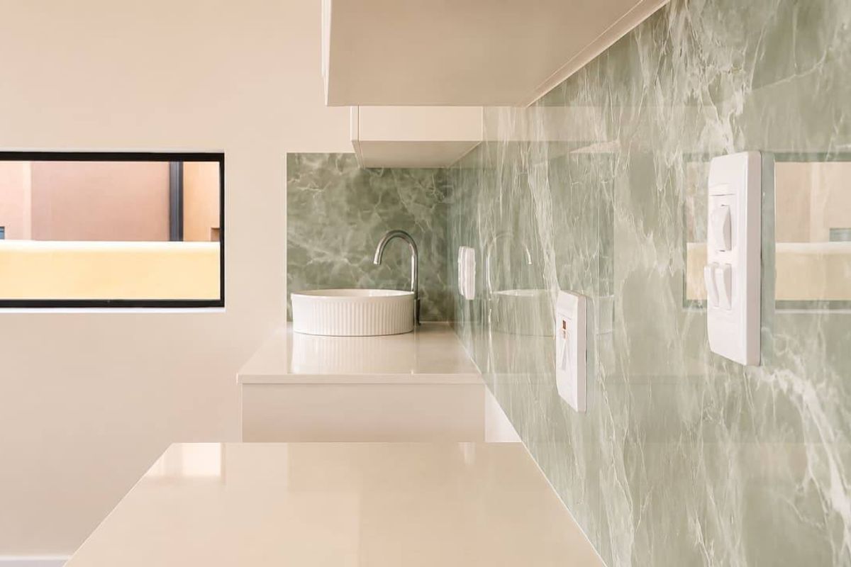 A modern kitchen area featuring a sleek stone countertop, elegant marble-look splashback, and a contemporary basin with a mixer tap.